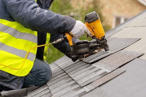 Tech installing shingles on a roof